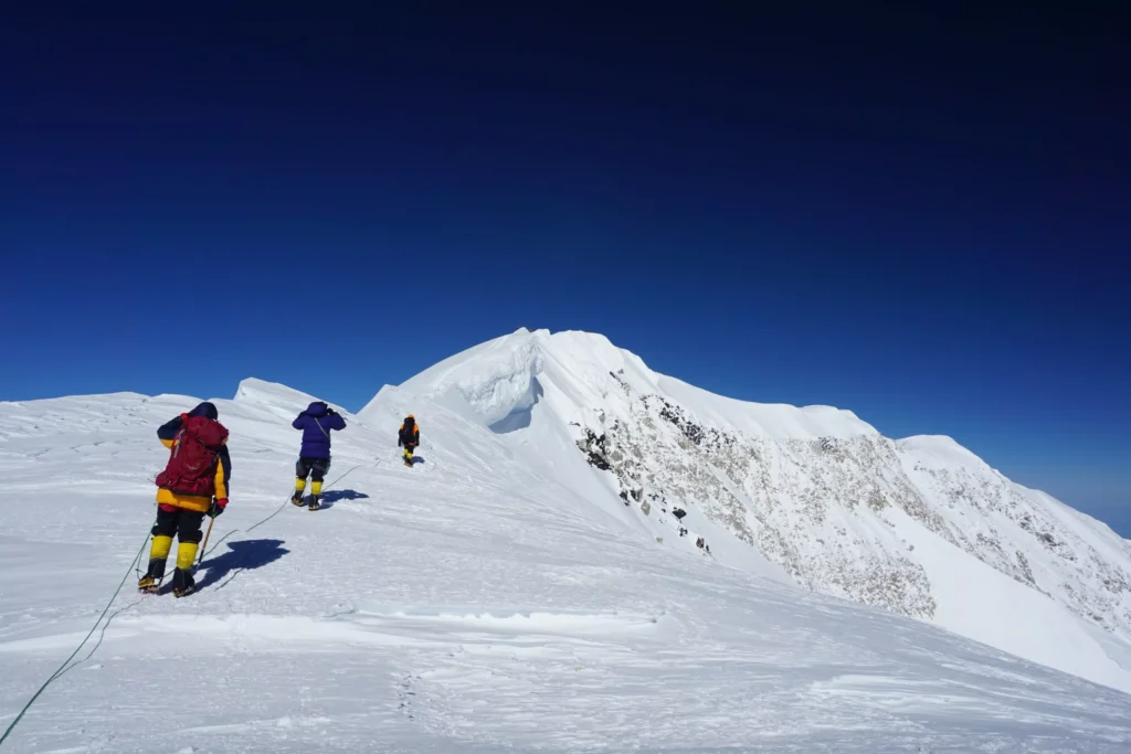 Atak szczytowy Denali – wspinacz z czekanem na tle chmur i lodowców